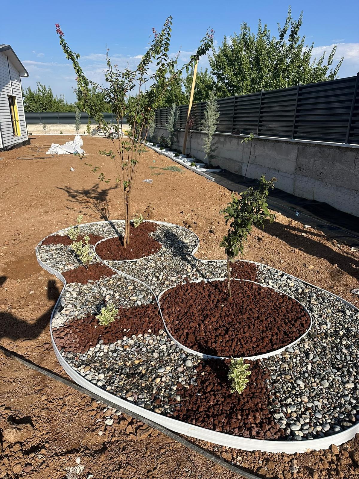 Yeni dikilen ağaçların dekoratif taşlarla çevrelendiği bahçe peyzaj adası